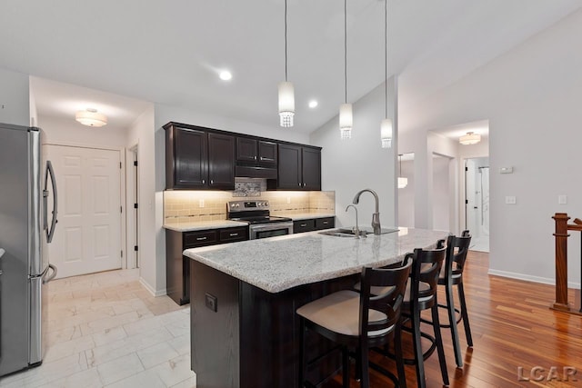 kitchen featuring lofted ceiling, sink, an island with sink, light stone counters, and stainless steel appliances