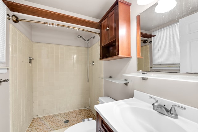 bathroom featuring toilet, a tile shower, and vanity