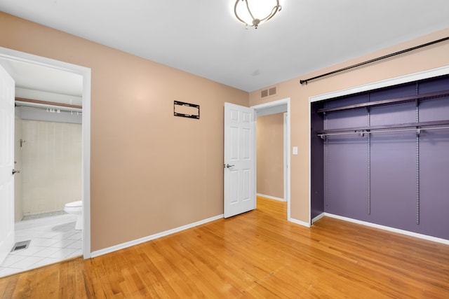 unfurnished bedroom featuring ensuite bath, a closet, and hardwood / wood-style floors