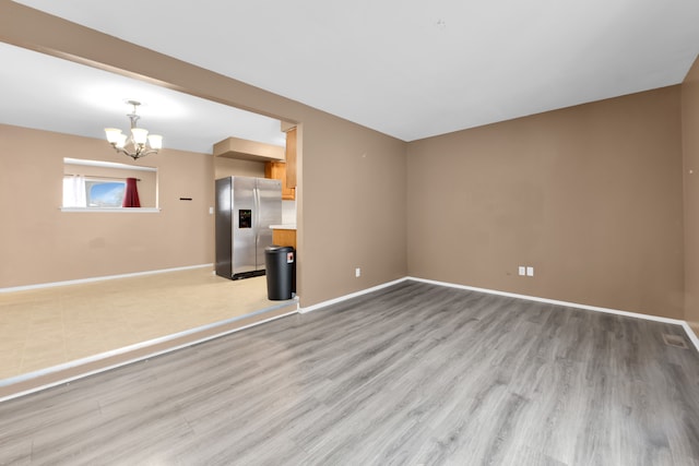 unfurnished living room featuring an inviting chandelier and light hardwood / wood-style floors