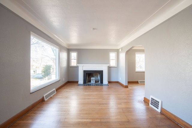 unfurnished living room with light hardwood / wood-style floors, a wealth of natural light, and crown molding