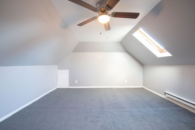 additional living space featuring ceiling fan, vaulted ceiling with skylight, a baseboard radiator, and dark carpet