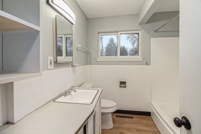 full bathroom with toilet, hardwood / wood-style flooring, tile walls, shower / bathtub combination, and vanity