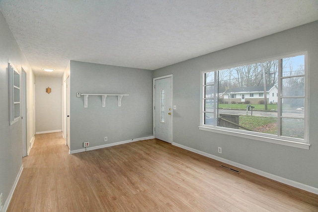 unfurnished room with light wood-type flooring and a textured ceiling