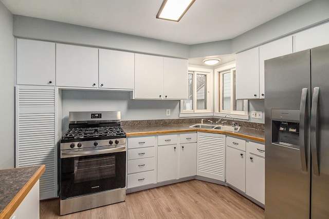 kitchen with appliances with stainless steel finishes, sink, white cabinetry, and light hardwood / wood-style flooring