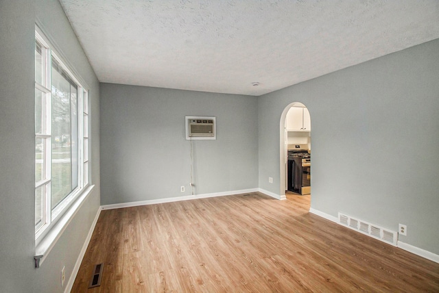 spare room featuring a wall unit AC, a textured ceiling, a healthy amount of sunlight, and light hardwood / wood-style floors