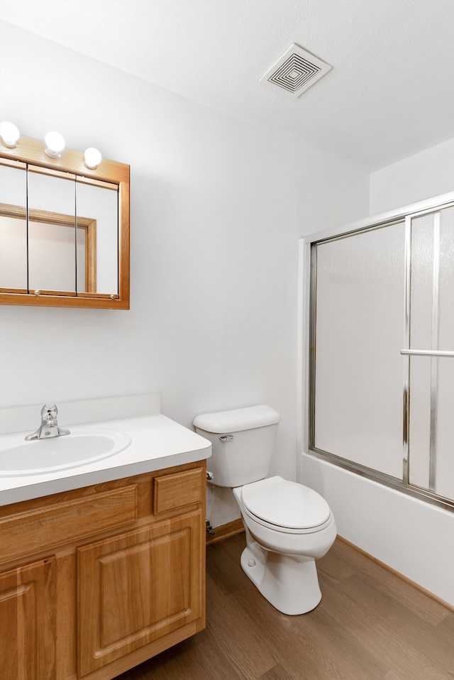 full bathroom with shower / bath combination with glass door, hardwood / wood-style flooring, toilet, and vanity