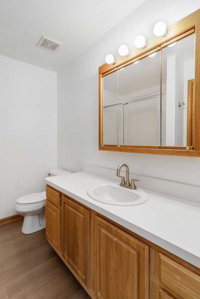 bathroom featuring toilet, wood-type flooring, vanity, and a shower with door