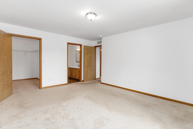 unfurnished bedroom featuring light colored carpet, a spacious closet, connected bathroom, and a closet