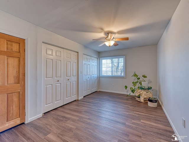 unfurnished bedroom featuring hardwood / wood-style flooring, ceiling fan, and multiple closets