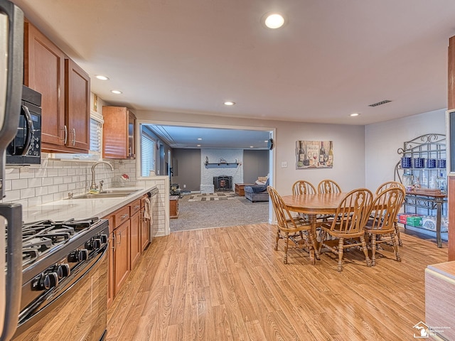 kitchen featuring decorative backsplash, light wood-type flooring, a brick fireplace, sink, and black appliances