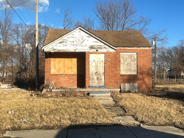 bungalow featuring a shingled roof and brick siding