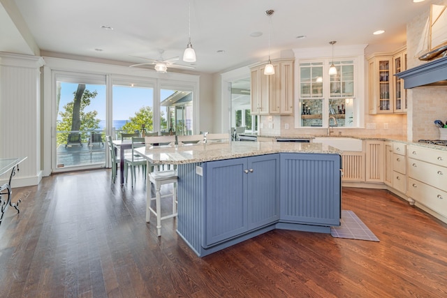 kitchen with a kitchen island with sink, glass insert cabinets, a sink, and decorative light fixtures