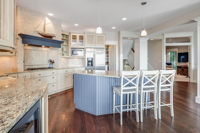 kitchen with glass insert cabinets, built in appliances, hanging light fixtures, light stone countertops, and a kitchen bar