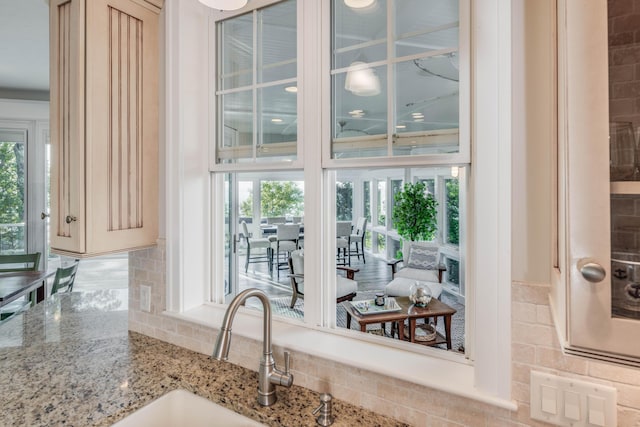 details featuring light stone counters, a sink, glass insert cabinets, and tasteful backsplash