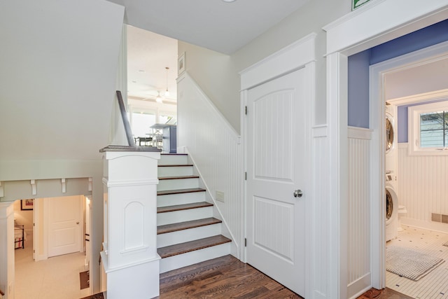 stairs featuring a wainscoted wall, wood finished floors, visible vents, and stacked washer / drying machine