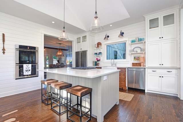 kitchen with wood walls, a center island, decorative light fixtures, white cabinetry, and stainless steel appliances