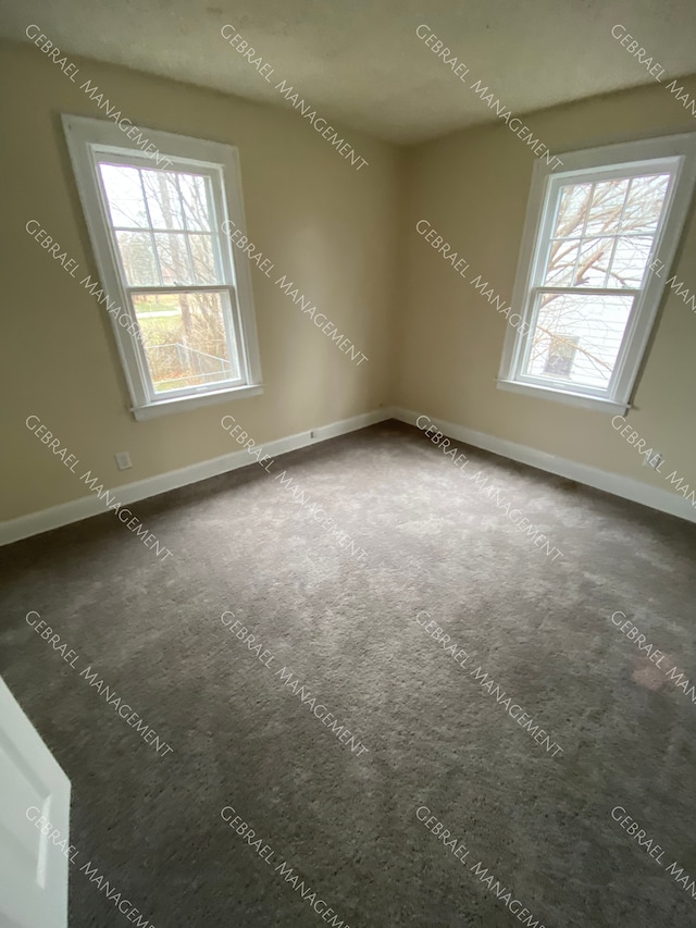 spare room featuring a healthy amount of sunlight and dark colored carpet