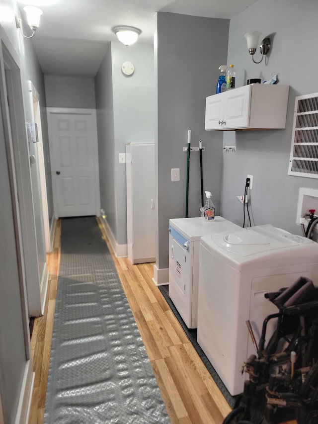 laundry room featuring independent washer and dryer, cabinets, and light hardwood / wood-style flooring