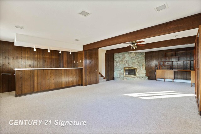 unfurnished living room with a stone fireplace, wood walls, beamed ceiling, and ceiling fan