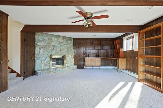 unfurnished living room with beam ceiling, ceiling fan, wood walls, light carpet, and a fireplace