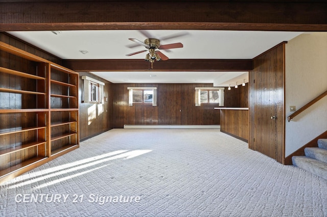 unfurnished living room featuring light colored carpet, baseboard heating, ceiling fan, beamed ceiling, and wood walls