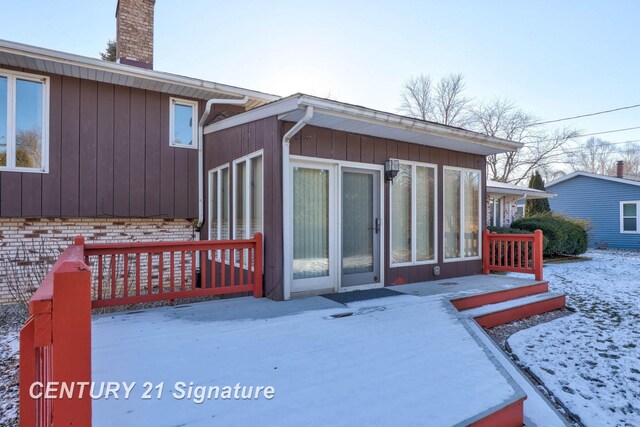 snow covered rear of property featuring a sunroom