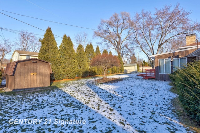 yard layered in snow featuring a storage shed and a deck