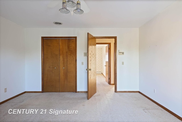 unfurnished bedroom featuring baseboard heating, light carpet, and a closet