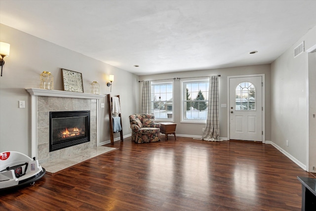 living area featuring a tiled fireplace and dark wood-type flooring