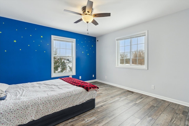 bedroom featuring a ceiling fan, visible vents, baseboards, and wood finished floors