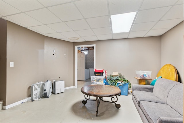 living room with a drop ceiling, concrete floors, and baseboards