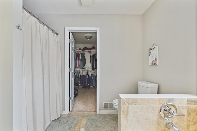 bathroom featuring visible vents, a walk in closet, and toilet