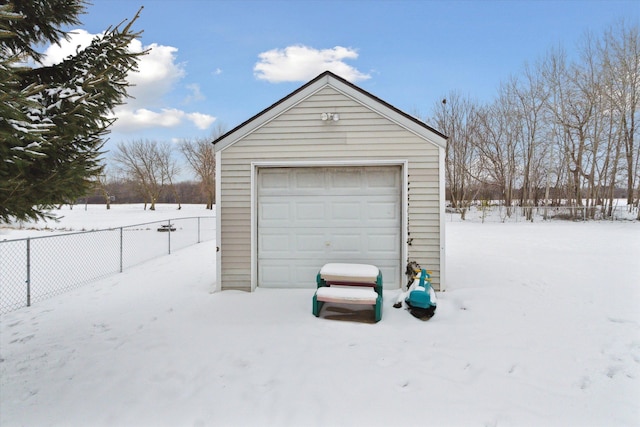 snow covered garage featuring a garage and fence