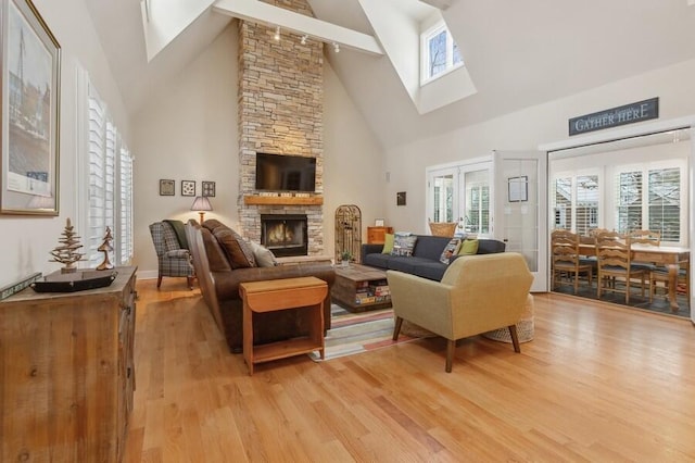 living room featuring a skylight, a fireplace, high vaulted ceiling, and light hardwood / wood-style flooring