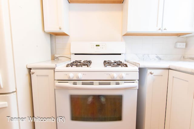 kitchen with white appliances, decorative backsplash, and white cabinets