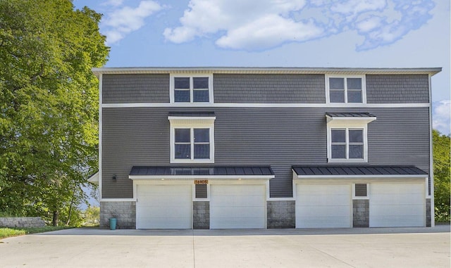 16905 Highland Ave, Spring Lake, MI 49456 - rear view of house featuring stone siding, an attached garage, concrete driveway, a standing seam roof, and metal roof