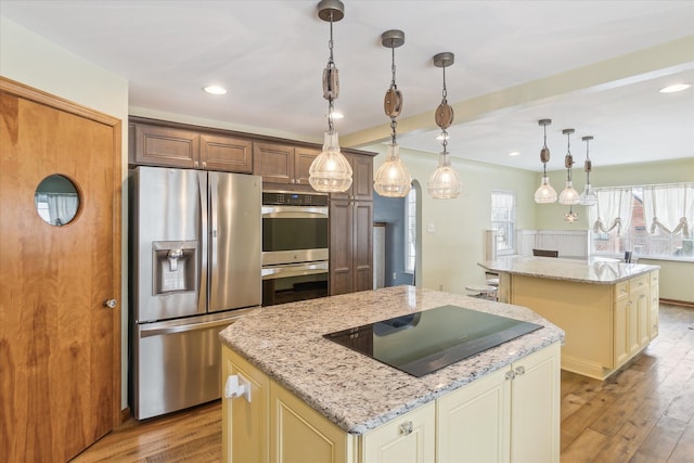 kitchen featuring light stone countertops, stainless steel appliances, cream cabinets, pendant lighting, and a kitchen island