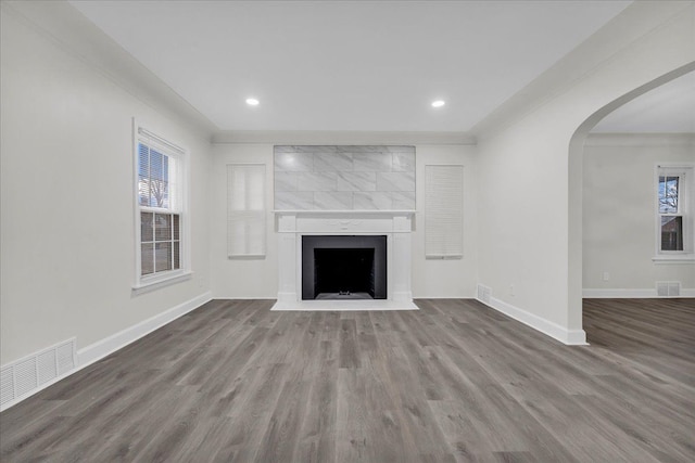 unfurnished living room featuring a large fireplace, a healthy amount of sunlight, wood-type flooring, and ornamental molding