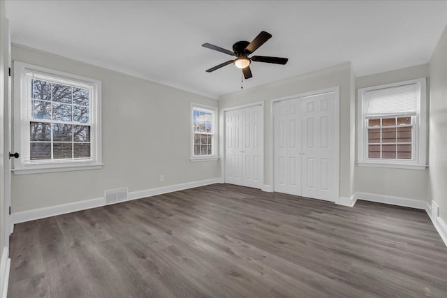 unfurnished bedroom featuring multiple closets, dark hardwood / wood-style floors, and ceiling fan