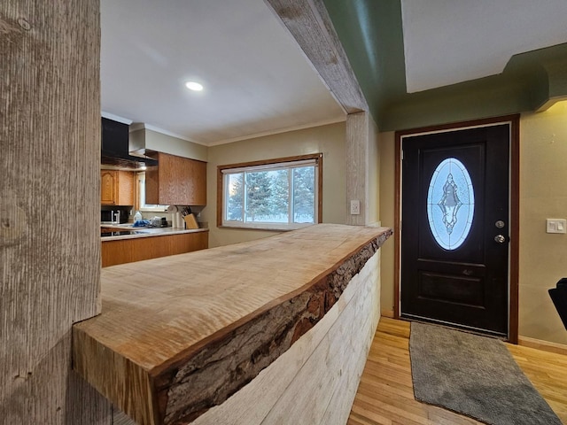 kitchen with kitchen peninsula, black gas stovetop, crown molding, and light hardwood / wood-style floors