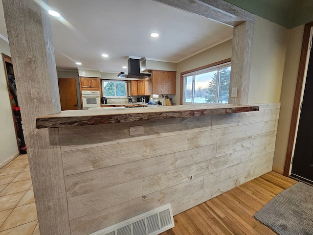 kitchen featuring kitchen peninsula, ornamental molding, oven, and wall chimney exhaust hood