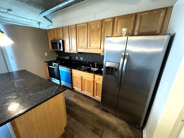 kitchen with backsplash, sink, dark stone countertops, appliances with stainless steel finishes, and dark hardwood / wood-style flooring