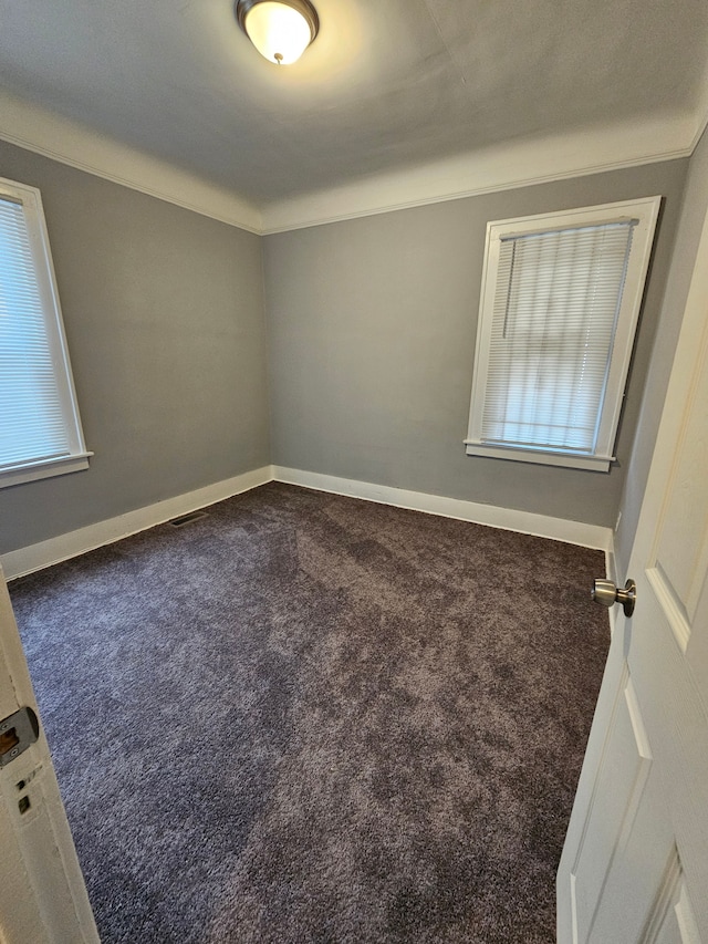 empty room with crown molding and dark colored carpet