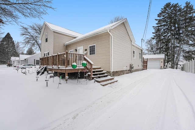 snow covered property featuring an outbuilding, a garage, and a wooden deck