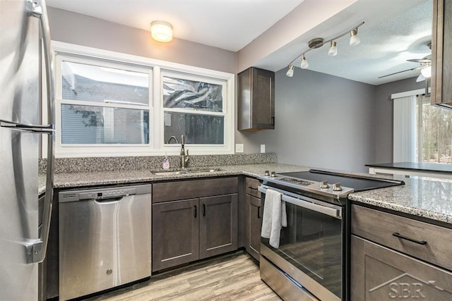 kitchen with sink, ceiling fan, light stone countertops, appliances with stainless steel finishes, and light hardwood / wood-style floors