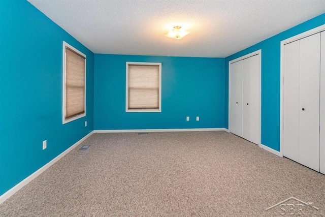 unfurnished bedroom featuring carpet flooring, multiple windows, a textured ceiling, and two closets