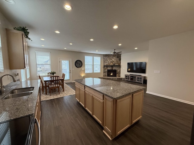 kitchen with sink, dark wood-type flooring, a stone fireplace, dark stone counters, and light brown cabinetry