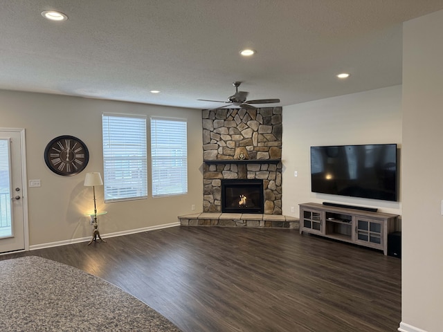 unfurnished living room with a textured ceiling, dark hardwood / wood-style flooring, a stone fireplace, and ceiling fan