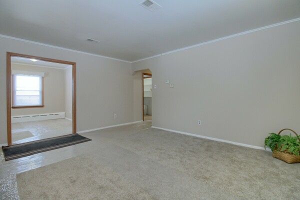 unfurnished living room featuring ornamental molding and a baseboard heating unit